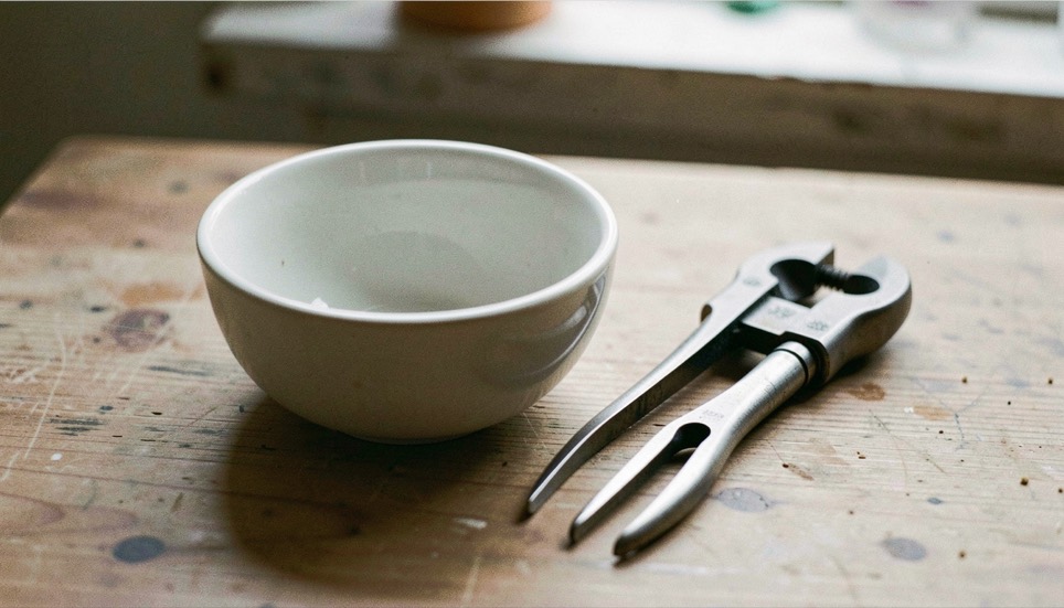 A small bowl progresses from square blank to rounded form beside a bowl gouge and curved calipers